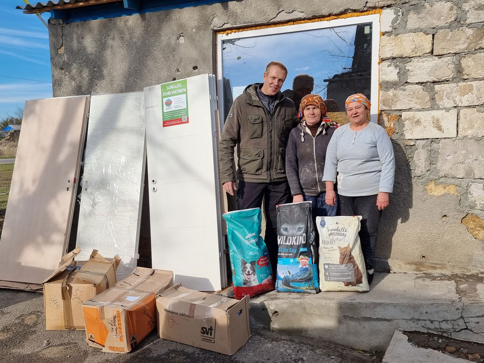 Übergabe von Türen, Baumaterial und Tierfutter an Bewohnerinnen eines beschädigten Hauses in der Südukraine