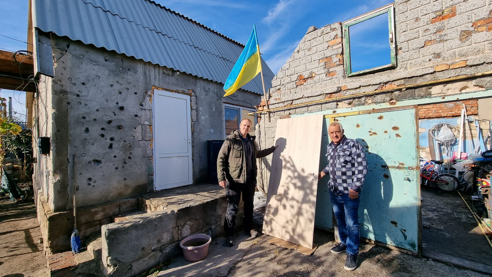 Übergabe einer neuen Haustür an einen Bewohner vor seinem vom Krieg beschädigten Haus in einem ukrainischen Dorf